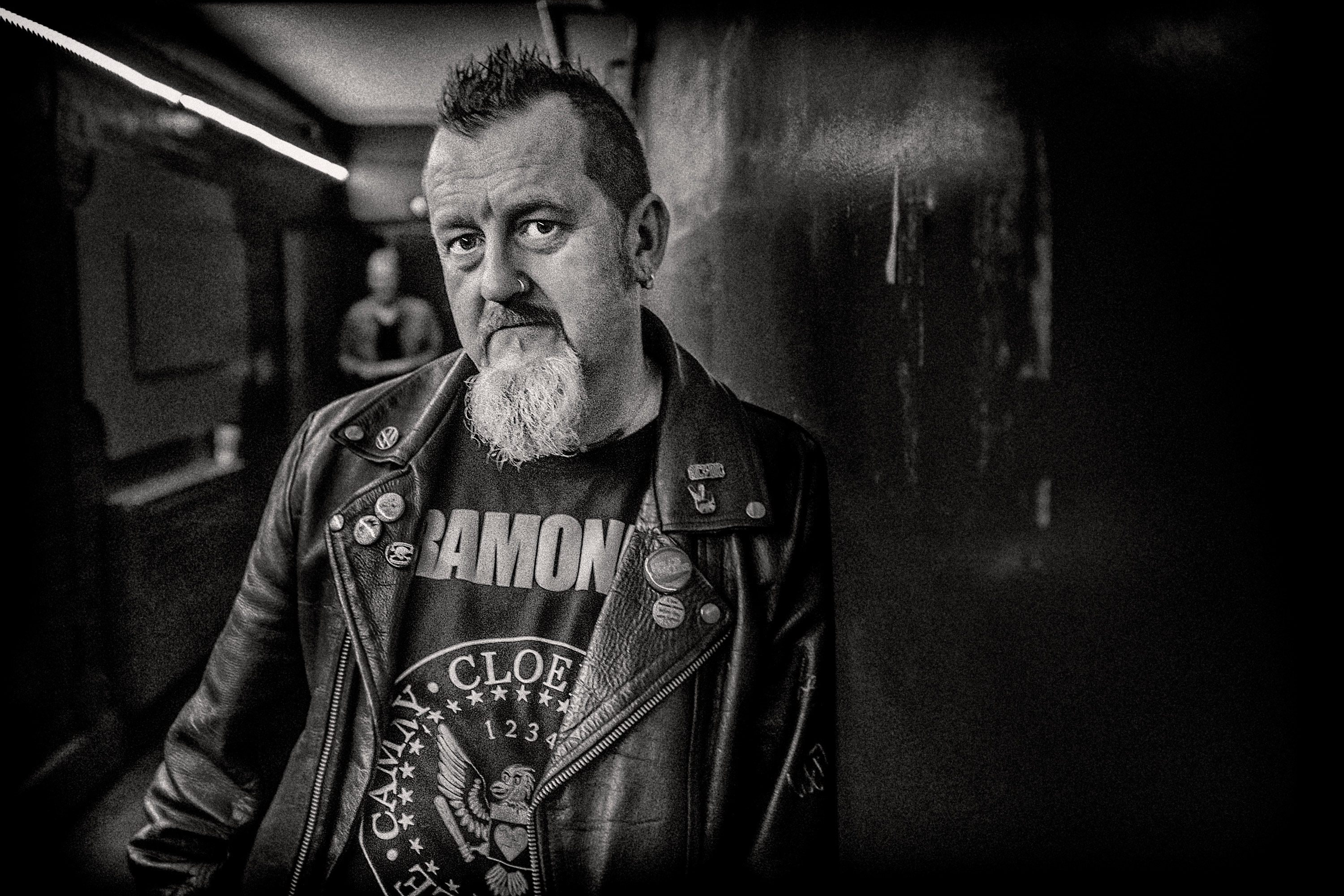 An atmospheric black and white portrait of a man wearing a leather jacket and Ramones t-shirt at a gig